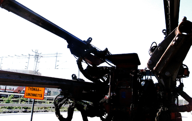 Eine Maschine ist im Vordergrund mit Strommasten, Kabeln, Barrieren, Pflanzen und Himmel im Hintergrund positioniert.