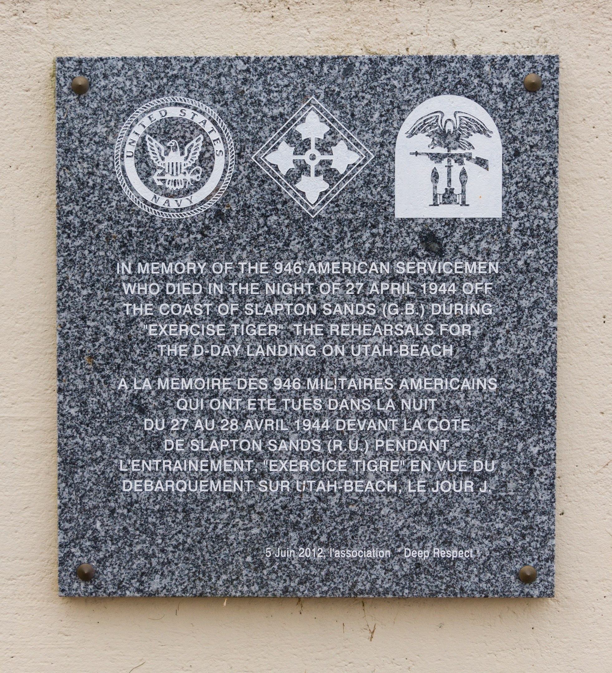 Stone plaque on a building's exterior engraved with "In Memory of the 946 American Servicemen" and logos.