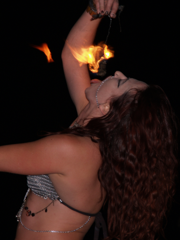 Eine Frau beugt sich über einen Ort und versucht, ein brennendes Objekt in ihrer Hand zu essen.