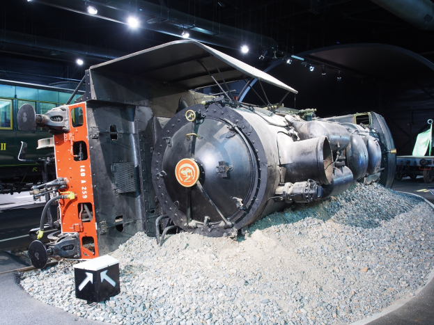 Eine alte Dampflokomotive in einem Museum ausgestellt, umgeben von Steinen und beleuchtet von Deckenlampen.