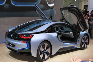 Ein BMW i8-Konzeptfahrzeug, das auf der Frankfurter Motor Show ausgestellt wird, umgeben von Menschen, mit einer Person, die im Vordergrund ein Mobiltelefon h├Ąlt, und verschiedenen Gegenst├Ąnden im Hintergrund.