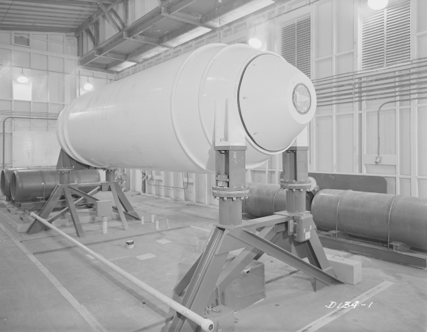 Großer zylindrischer Wasserstoffbomben auf einem Ständer in einer industriellen Fabrikumgebung mit sichtbaren Rohren, Lampen und einer Wand im Hintergrund.