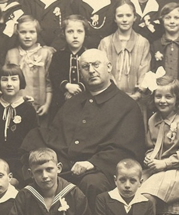 Ein Schwarz-Weiß-Foto eines ernst aussehenden Mannes, der in der Mitte sitzt und von einer Gruppe bewundernder Kinder umgeben ist.