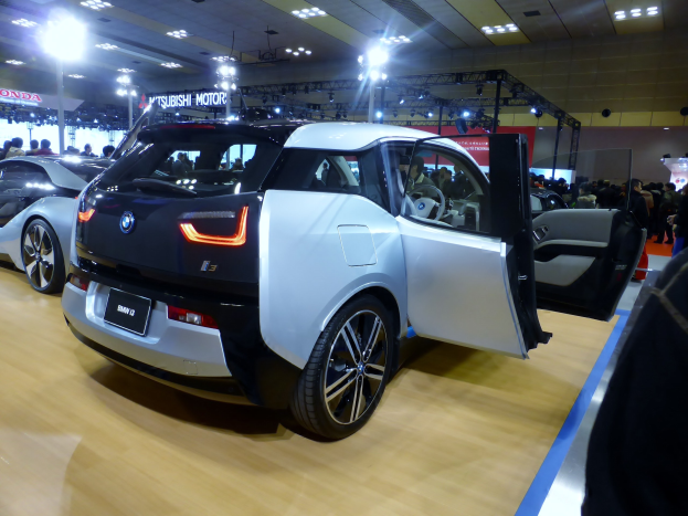 Ein weißes und schwarzes BMW i3 Elektroauto auf der IAA in Frankfurt, umgeben von Menschen und beleuchtet von Deckenlampen, mit Informationsschildern im Hintergrund.