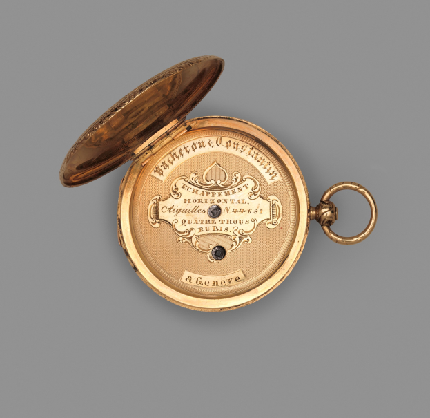 Eine goldene Taschenuhr mit geschlossenem Deckel auf einem grauen Hintergrund, mit eingravierter Schrift.