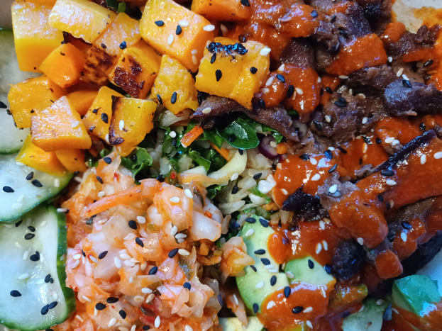 Ein Nahaufnahme einer Schüssel mit farbenfrohen Gemüsen wie Karotten, Paprika, Zwiebeln und Pilzen, fluffigem weißem Reis und goldbraunem, saftigem Fleisch.