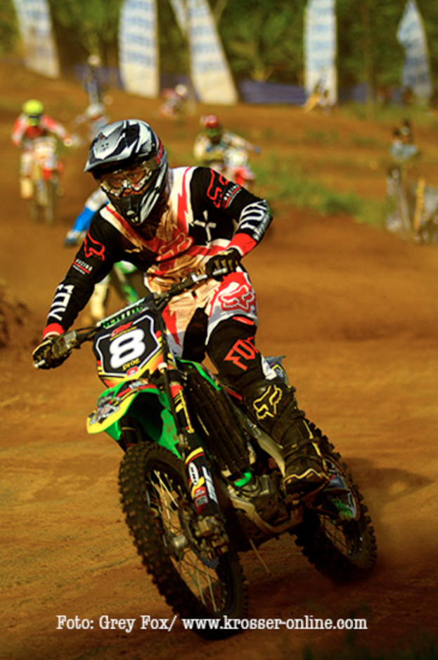 Mehrere Motorradfahrer mit Helmen rennen, mit Text am unteren Bildrand.