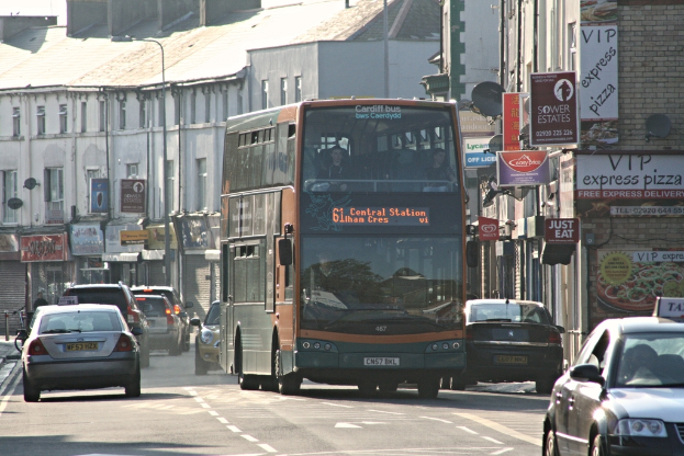 Eine StraÃe mit Autos und einem Bus, GebÃ¤ude mit WÃ¤nden, Fenstern, Tellern und DÃ¤chern, Plakate und Banner an den WÃ¤nden und ein Mast mit einer StraÃenlaterne.