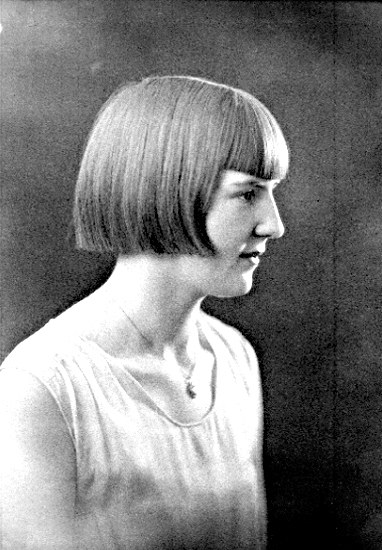 Ein Schwarz-Weiß-Foto einer Frau mit einem kurzen Bob-Haarschnitt, ihr Gesicht ist deutlich zu sehen, mit Blick zur Seite und leicht geöffneten Lippen.