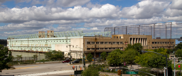 Eine Straße mit Fahrzeugen, Bäumen und Straßenlaternen, die zu einem großen Gebäude in der Nähe eines Gewässers führt.