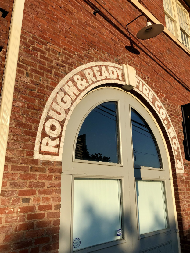 Ziegelgebäude mit einer Glastür, Fenstern, einer Lampe und einem "Rough & Ready Fire Co." -Schild.