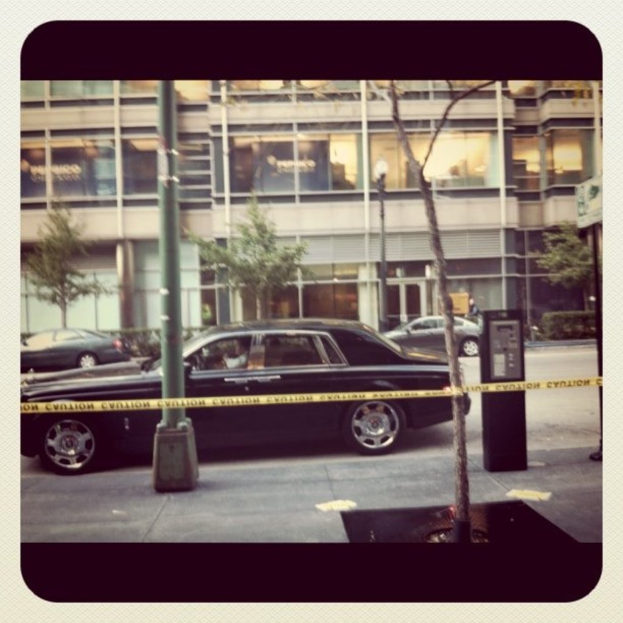 Ein Auto ist auf dem Bild in der Mitte mit Pfosten und Bäumen geparkt, mit einem Gebäude, Fahrzeugen, Bäumen, Pflanzen und Lichtern im Hintergrund und einem Weg am Boden.