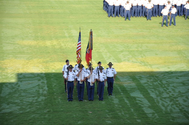 Eine Gruppe von Jungs in weiÃŸ-blauen Uniformen steht in einer Reihe auf einem grÃ¼nen Feld, zwei Jungs vorne halten Fahnen.