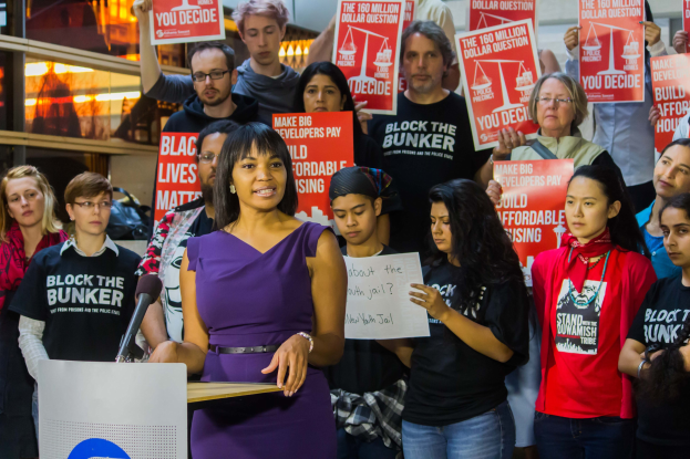 Eine Black-Lives-Matter-Aktivistin, die vor einer Menge mit Schildern spricht, mit Mikrofon und anderen Gegenständen im Hintergrund.