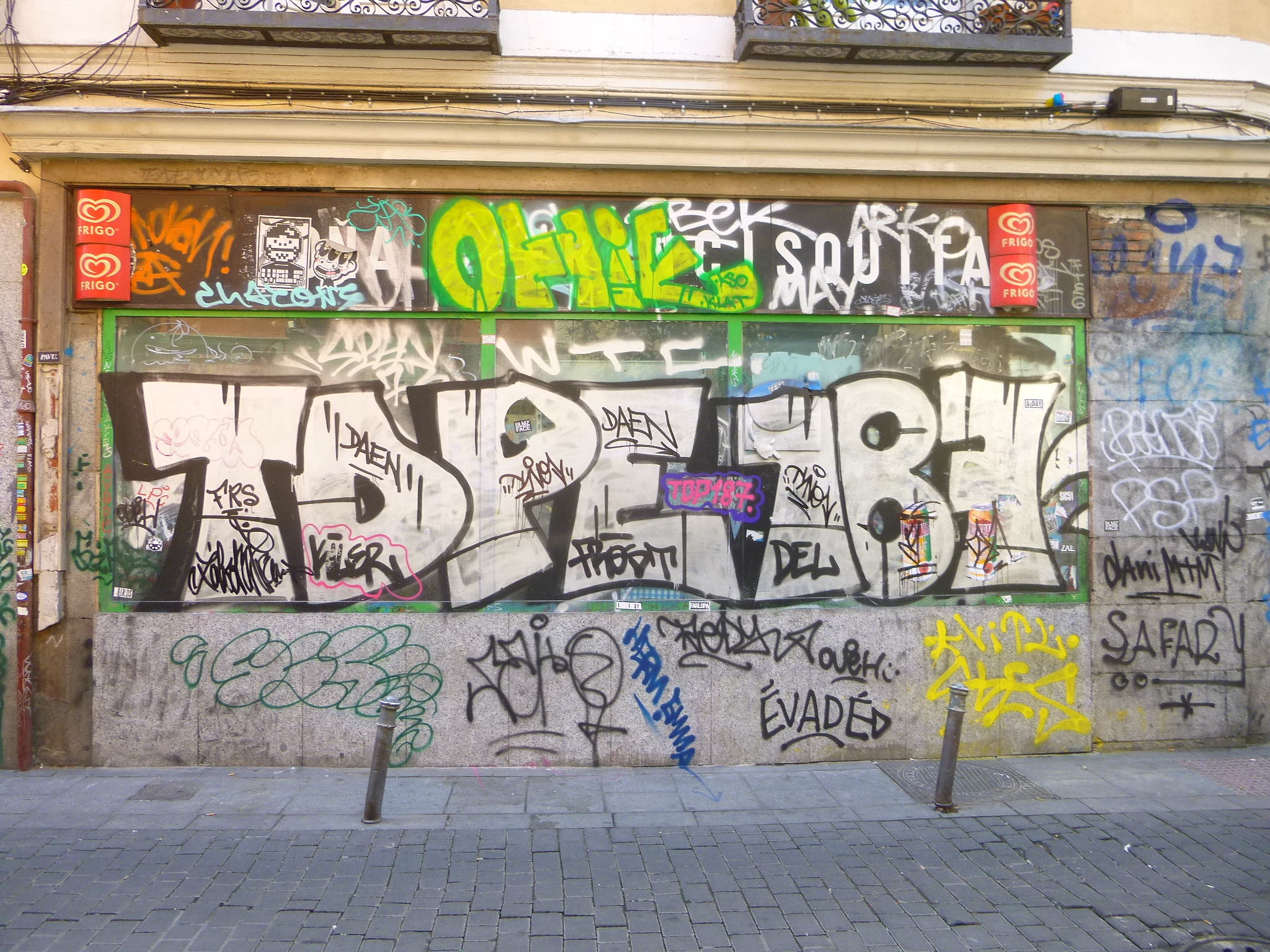 Ein Gebäude mit buntem, abwechslungsreichem Graffiti an der Seite, mit einer Straße, die unten von kleinen Pfählen gesäumt ist.