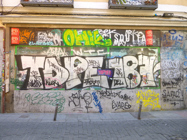 Ein Gebäude mit buntem, abwechslungsreichem Graffiti an der Seite, mit einer Straße, die unten von kleinen Pfählen gesäumt ist.