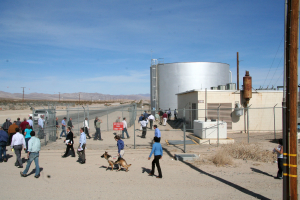 Eine spärliche Szene mit ein paar Menschen, die herumstreifen, einem Hund, Häusern, Zaunpfählen und einem Himmel darüber.