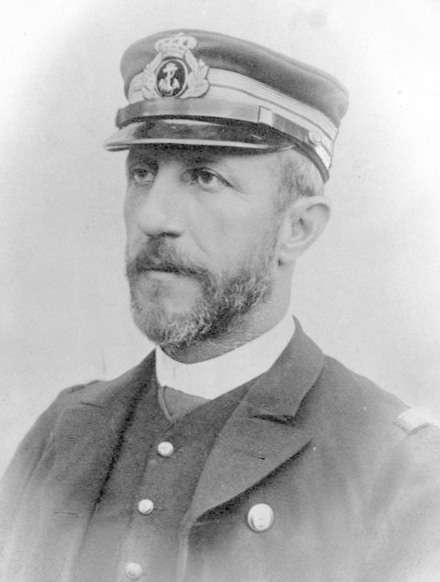 Ein Schwarz-Weiß-Foto eines Mannes in Uniform, der eine Mütze und einen Mantel trägt und einen strengen Gesichtsausdruck hat, der darauf hindeutet, dass er ein Kapitän ist.