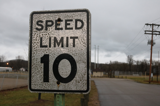 Tempo-Begrenzungsschild am Straßenrand mit Gras, Strommasten, Häusern, Bäumen und einem bewölkten Himmel.