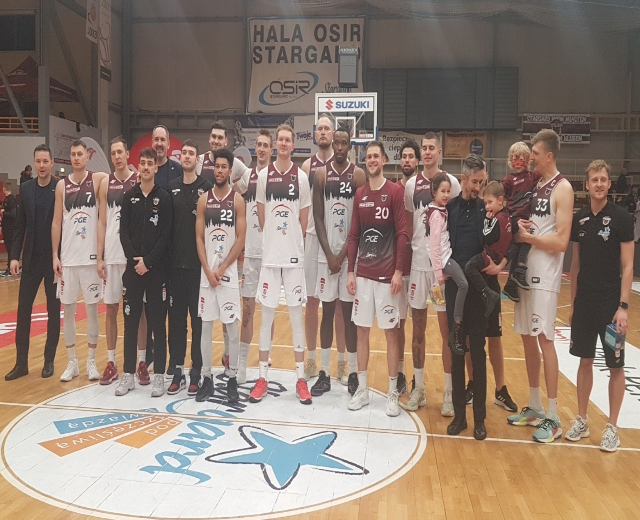 Gruppe von Männern und Kindern auf einem Basketballfeld mit Schildern im Hintergrund.