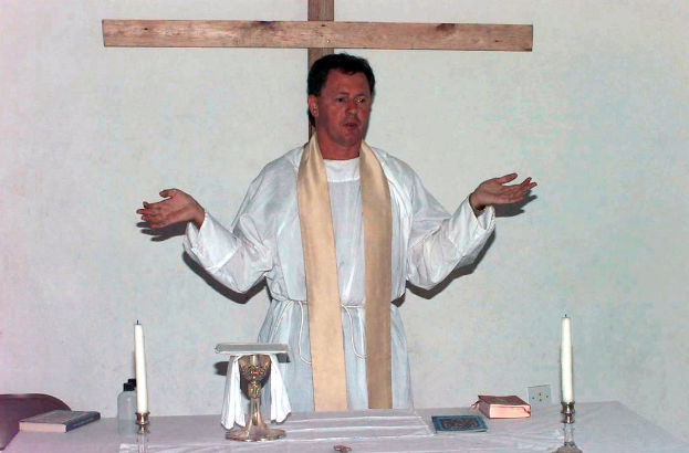 Ein Priester steht an einem Tisch mit Kerzen und Büchern vor ihm.