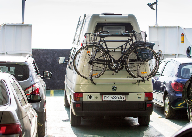 Mehrere Fahrzeuge, darunter Autos und Fahrräder in verschiedenen Farben, sind in der Mitte des Bildes positioniert.