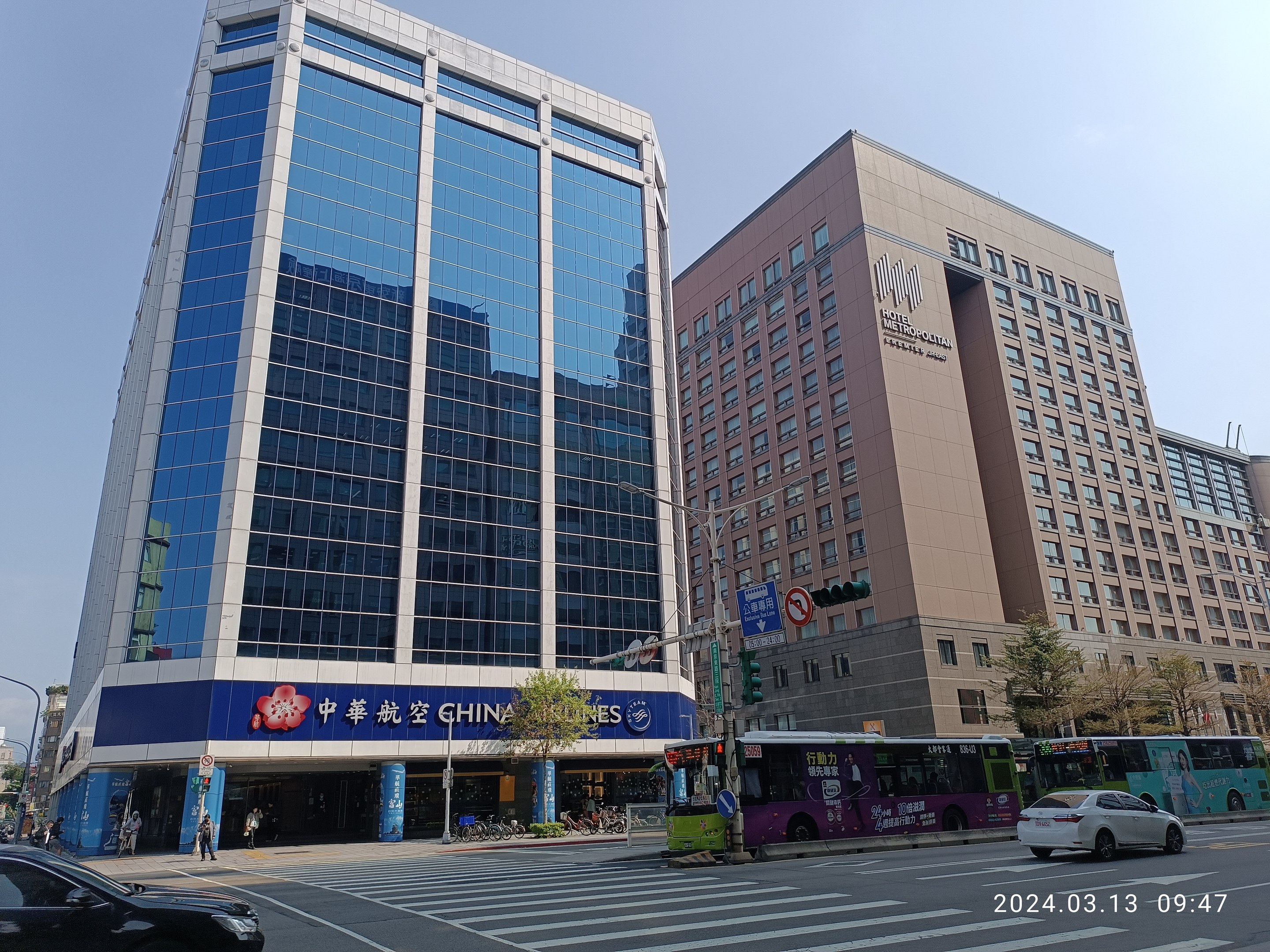 Stadtstraße mit Fahrzeugen, Fußgängern und hohen Gebäuden in Peking, mit Verkehrszeichen, Schildern, Bäumen und Laternen unter einem sichtbaren Himmel.