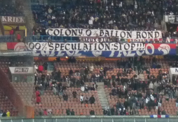 Ein Stadion mit einer großen Menschenmenge, Schildern und Stühlen, mit einem Zaun unten und Treppen auf der linken Seite.