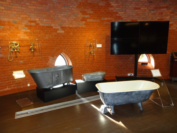 Ein gemütliches Badezimmer mit einer Ziegelwand, einer zentralen Badewanne, an der Wand angebrachten Hähnen auf der linken Seite und einem Fernseher auf der rechten Seite.