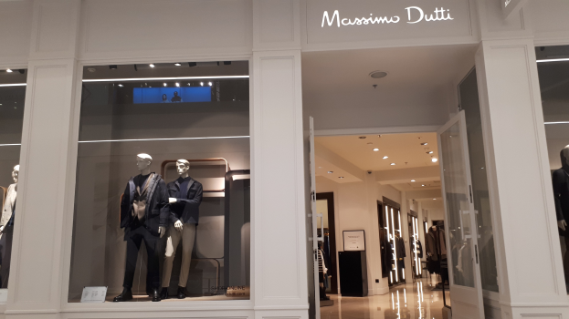 Vitrine des Massimo Dutti in Mailand, Italien, mit Schaufensterpuppen in moderner Kleidung, Innenbeleuchtung, Texttafeln und Türen mit sichtbarem Boden.