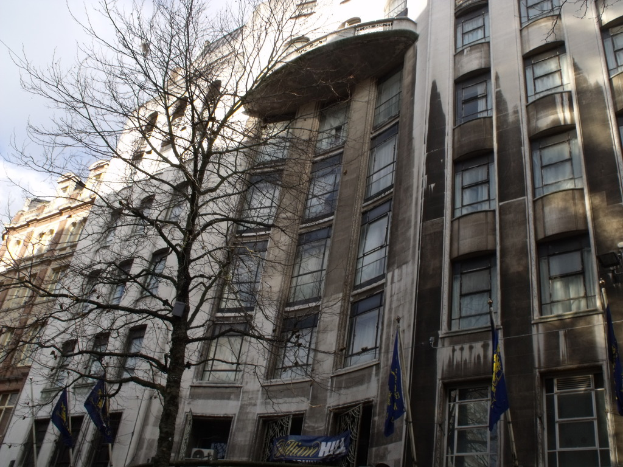 Gebäude mit Fenstern, einem Banner und Fahnen am Boden sowie einem Baum mit Ästen.