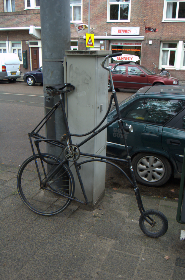 Ein Fahrrad steht in der N√§he einer Stra√üe mit Masten, Schildern, Fahrzeugen, Geb√§uden mit Fenstern und Gardinen sowie Flaggen.