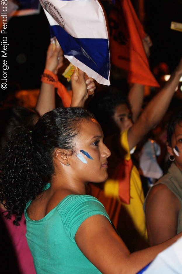 Frauen in grünen T-Shirts bei einer Demonstration, die weiße Decken halten, mit vielen anderen Mädchen im Hintergrund.