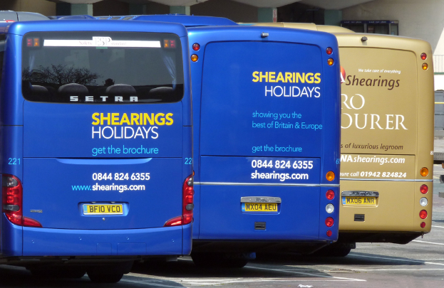 Drei Busse mit sichtbaren Nummernschildern, Lichtern und einem Glasobjekt vor einer Wand geparkt.