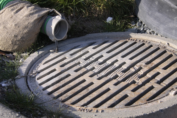 Ein Schlagloch mit Gras, Steinen, einer Tüte und einem Rohr auf der linken Seite und Gras, Steinen und einem Objekt oben.