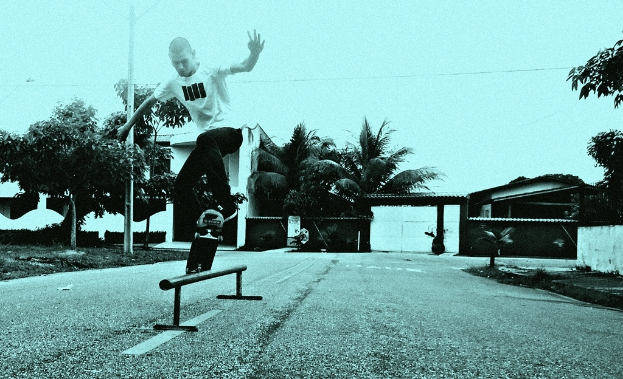 Eine Person Skateboard fahrend mit Bäumen und Gebäuden im Hintergrund.