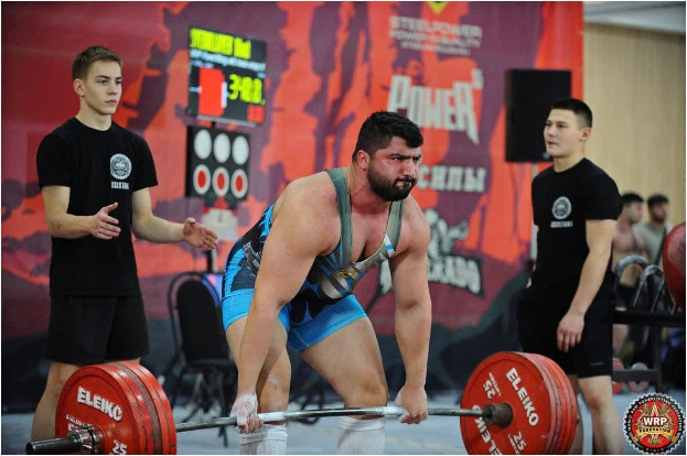 Ein Mann hebt eine Hantel bei einem Gewichtheben-Wettbewerb, umgeben von Zuschauern und Offiziellen, bei den World Weightlifting Championships 2018.