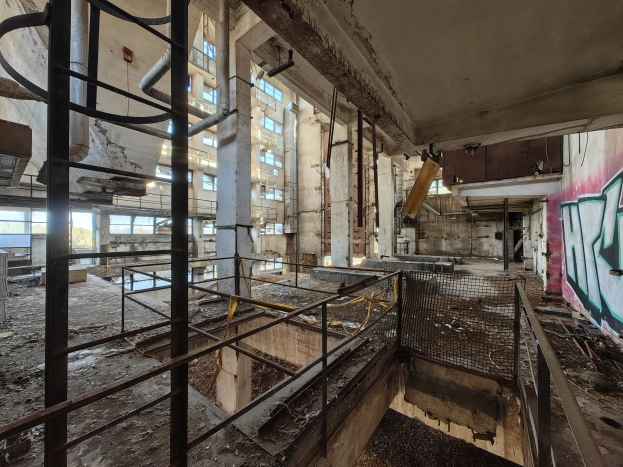 Verlassene Gebäudeinnenseite mit Graffiti-beschmierten Wänden, bröckelnden Strukturen, Geländern, Pfählen, Rohren und zerbrochenen Fenstern, mit einem Wasserzeichen unten.