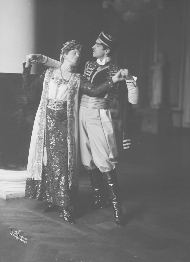 Schwarz-weiß-Foto eines Mannes und einer Frau, die in einem Ballsaal tanzen, mit einer Säule und einer Wand im Hintergrund; der Mann trägt Schuhe während ihrer Vorstellung.