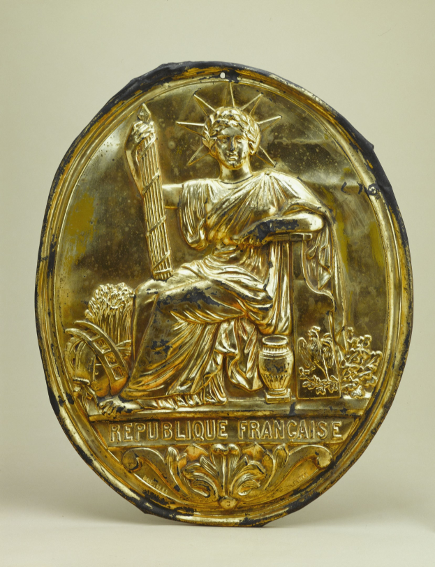 Goldenes rundes Schild mit einem Relief der Freiheitsstatue und eingraviertem Text auf einem weißen Hintergrund.