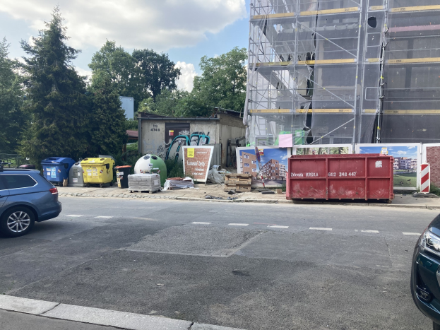 Zwei Autos neben einem Bauwerk geparkt mit verstreutem Schutt, Bäumen und einem bewölkten Himmel im Hintergrund.