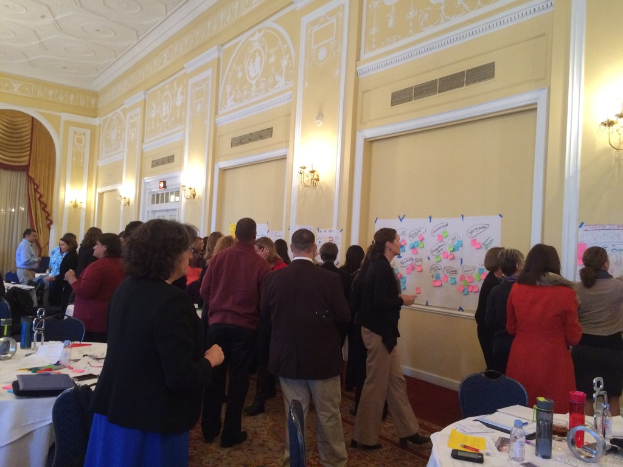 Eine Gruppe von Menschen, die Plakate und Charts auf einer Wand in einem Gebäude betrachten, das wie ein Kunstmuseum aussieht.