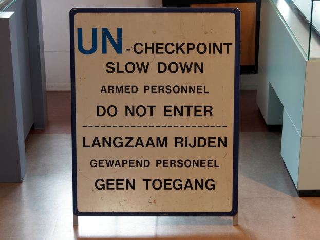 Ein Bodenaufkleber mit der Aufschrift "UN-Checkpoint Slow Down Armed Personnel - Do Not Enter" mit einer Glasplatte und Gegenständen im Hintergrund.