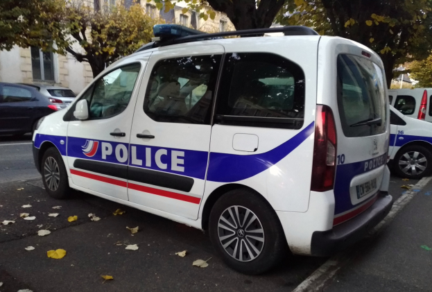 Ein Polizeifahrzeug auf einer von Gebäuden gesäumten Straße geparkt, umgeben von Bäumen und verstreuten Blättern auf dem Boden.