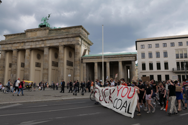 Menschen zu Fuß und mit dem Fahrrad am Brandenburger Tor in Berlin, die eine Fahne halten, mit Laternenpfählen und bewölktem Himmel.
