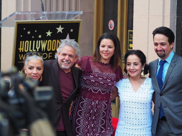 Gruppe von Menschen, die in der Nähe eines Hollywood Walk of Fame Stars posen, mit einem Podium und einem Mikrofon, einer Texttafel dahinter, einem Fotografen links und einer Tür im Hintergrund.