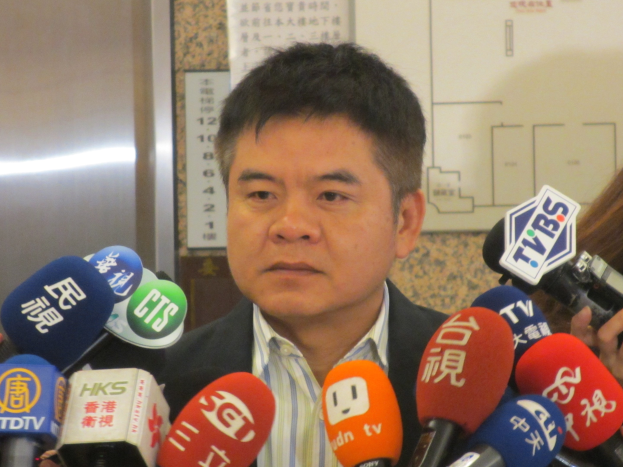 Mann im Anzug spricht mit Reportern, Frau mit Kamera rechts im Bild.