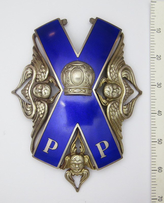 Ein blaues und silbernes Abzeichen mit einer Krone, das die Tapferkeitsmedaille des Vaterländischen Krieges darstellt, auf einem weißen Hintergrund neben einer Waage.