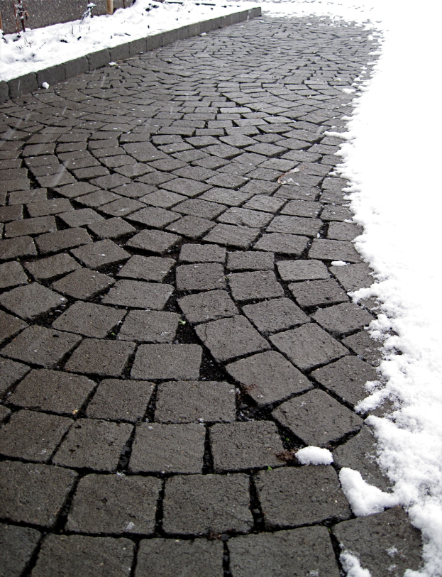 Ein Kopfsteinpflasterweg mit einer leichten Schneeschicht, ein Zaun ist im Hintergrund zu sehen.