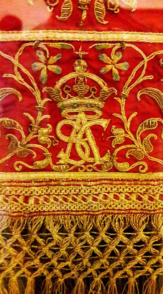 Close-up of a red and gold cloth featuring a crown and intricate gold embroidery.